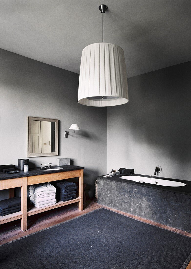 Ein monochromes Badezimmer mit Steinbadewanne und einfachem Holzwaschtisch