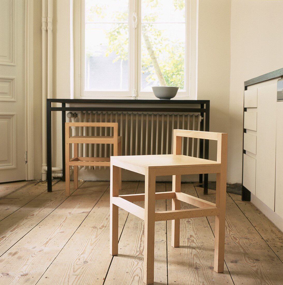 Ein einfacher Holzstuhl mit angedeuteter Rückenlehne in einer Küche mit altem Holzfußboden