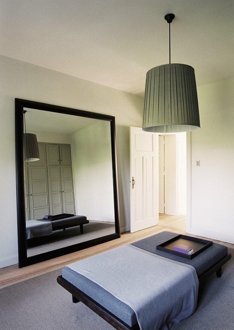 Ein eleganter Schlafraum mit breiter Polsterbank und großem, schwarz gerahmtem Spiegel