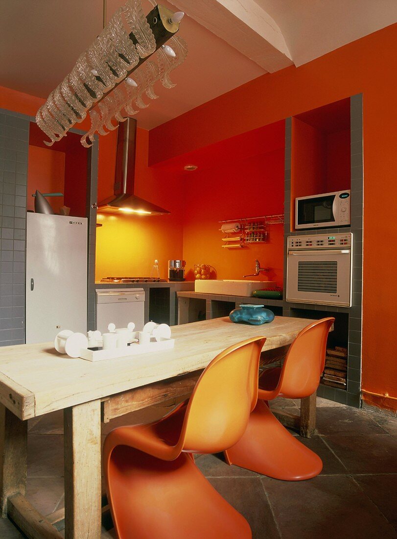 Zwei Panton Stühle an einem rustikalen Holztisch bilden den Höhepunkt der individuellen Küche mit roten Wänden und Stauraumnischen