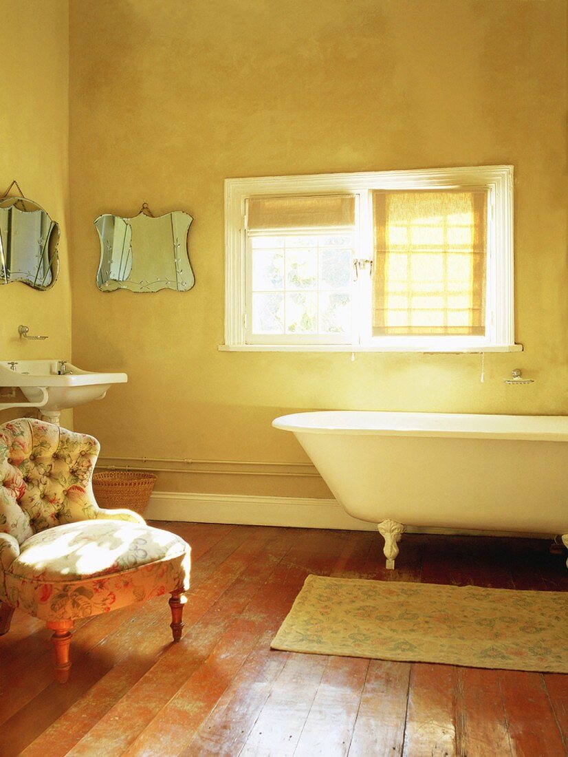 Eine Clawfoot Badewanne und ein romantischer Sessel in einem Badezimmer mit altem Dielenboden