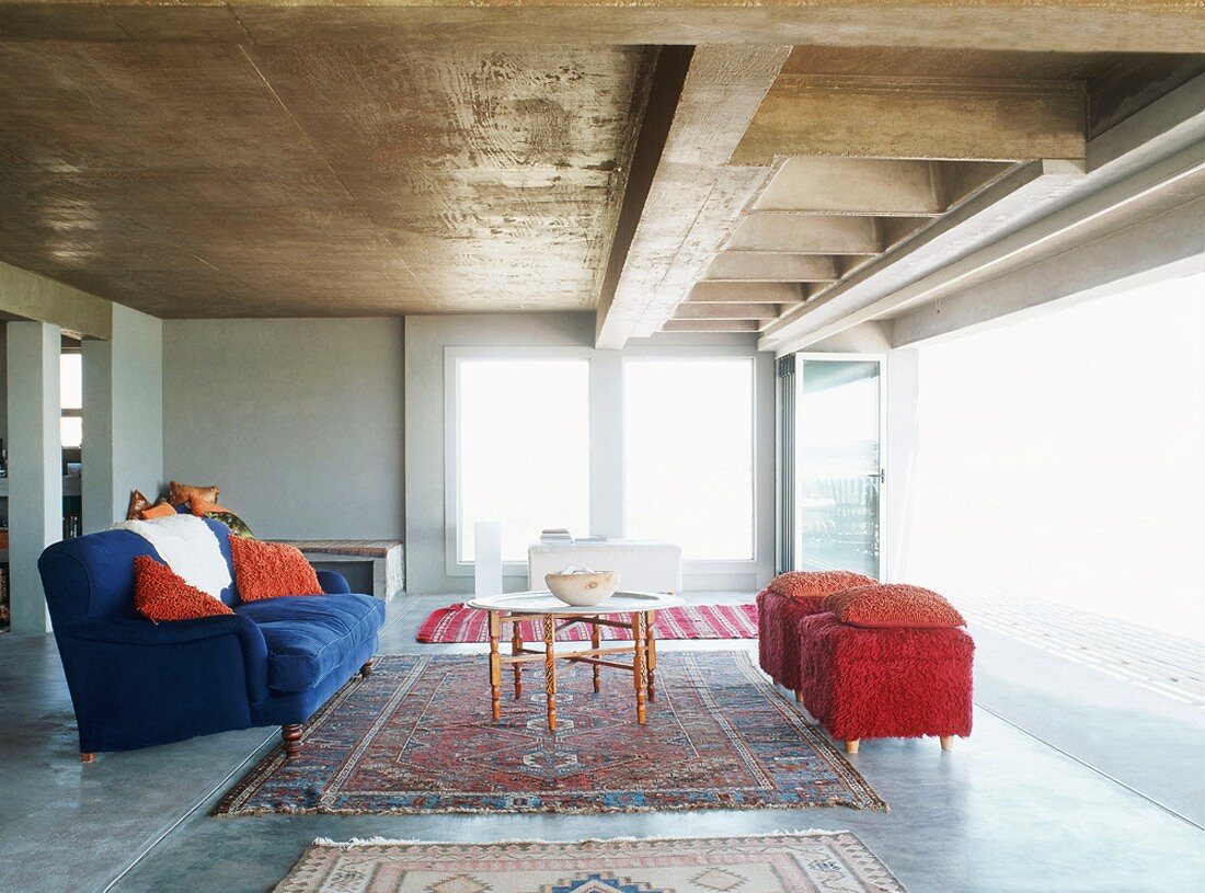 Orientteppiche und bunte Polstermöbel verleihen der kühlen Architektur mit Betondecke und Epoxidharzboden Wohnlichkeit
