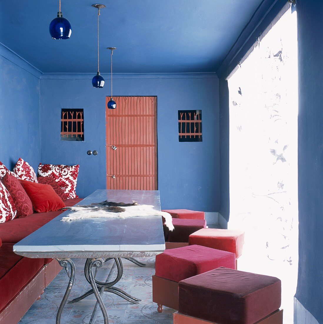 Schlichte, rote Polstermöbel an einem antiken Metalltisch bilden einen starken Kontrast zu dem blauen, traditionellen Wohnraum
