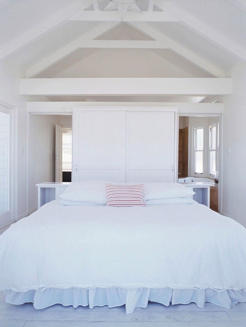 Ein schneeweisses Schlafzimmer mit Holzbalkendecke und großem Doppelbett