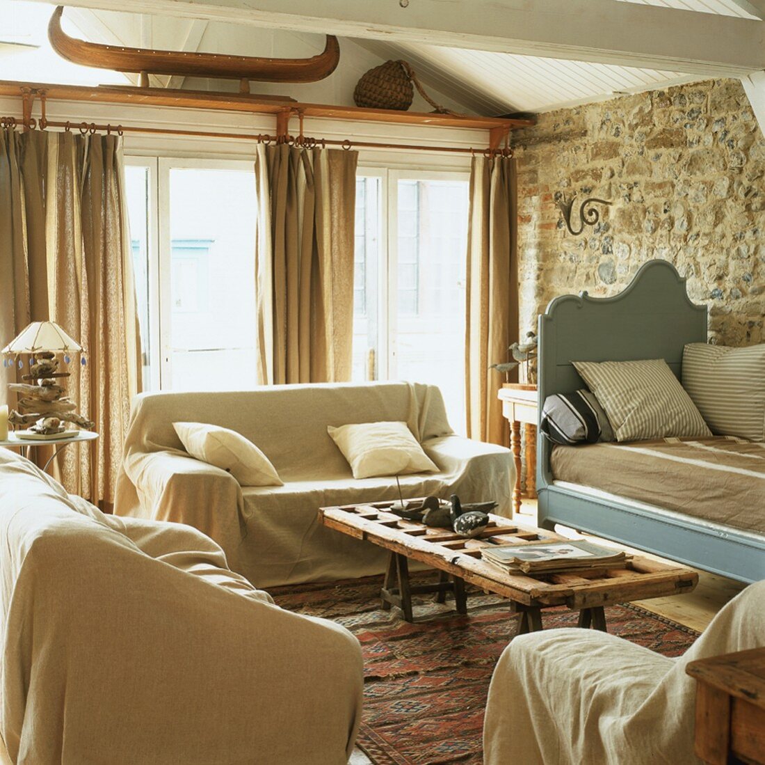 Rustikale Gemütlichkeit in einem Wohnzimmer mit Natursteinwand und weisser Holzbalkendecke