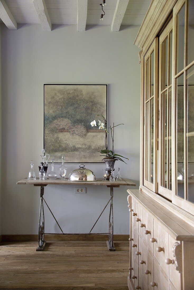 Glasfläschchen und Servierhaube auf einem filigranen, antiken Wandtisch und ein impressionistisches Gemälde
