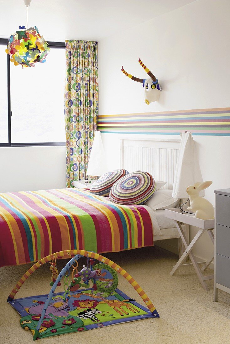 Bunt gestreifte Bettwäsche und Wandbordüre in einem aufgeräumten Kinderzimmer