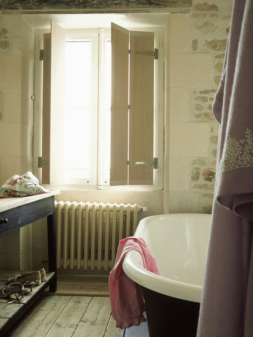 Rustikales Badezimmer mit antiker Badewanne und Waschtisch vor einem Fenster mit Holzläden
