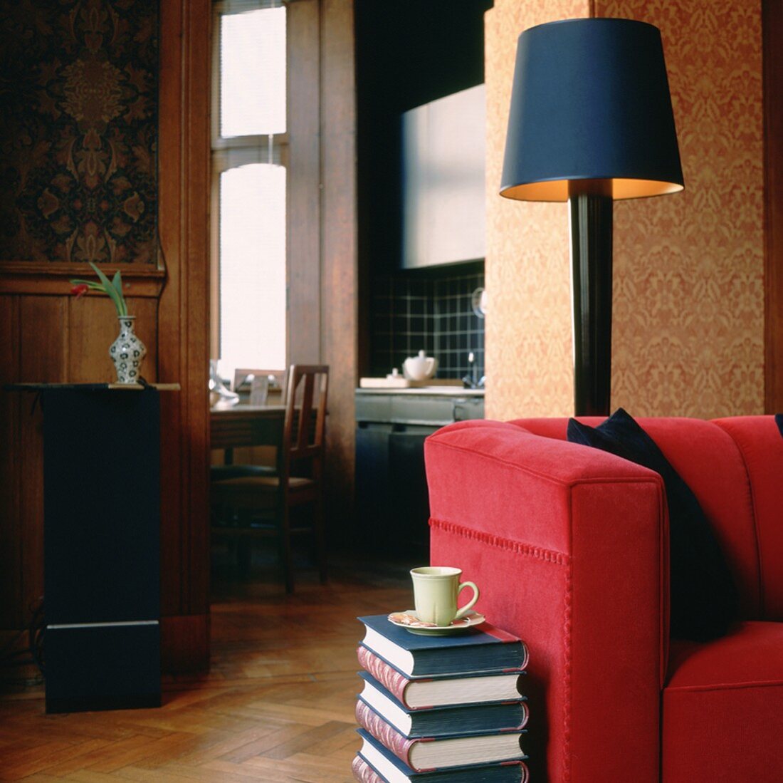 Wohnzimmerausschnitt mit rotem Sofa und Kaffeetasse auf einem Bücherstapel
