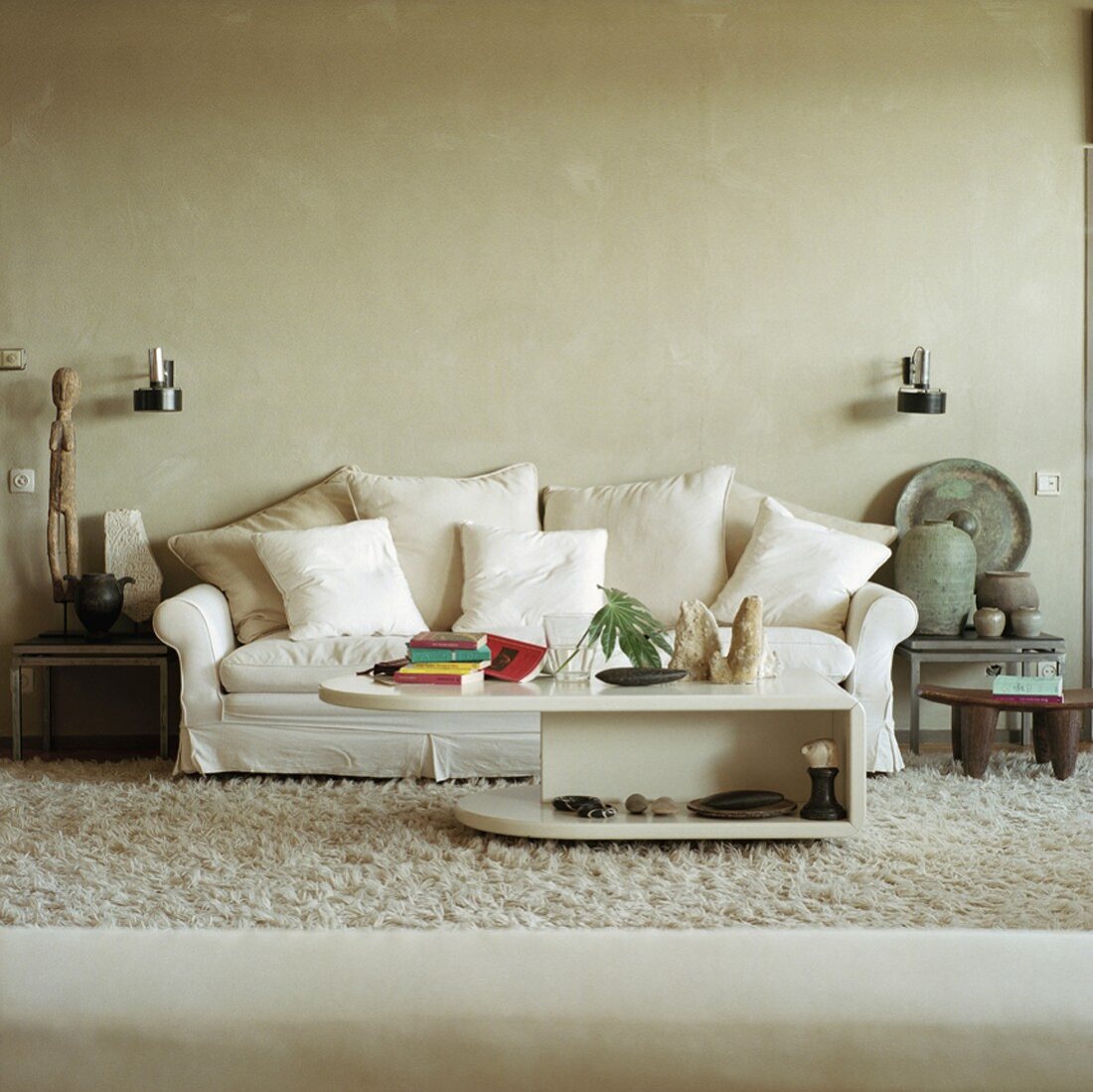 Weisses Sofa mit vielen Kissen und antike Tongefäße und Sklupturen auf Beistelltischen
