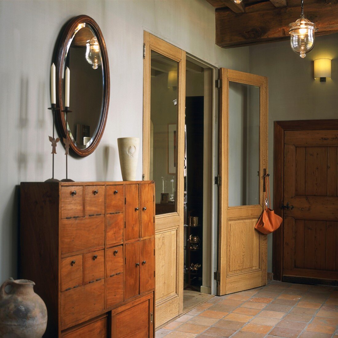 Antike Schubladenkommode unter ovalem Wandspiegel im rustikalen Hausflur mit verglaster Flügeltür