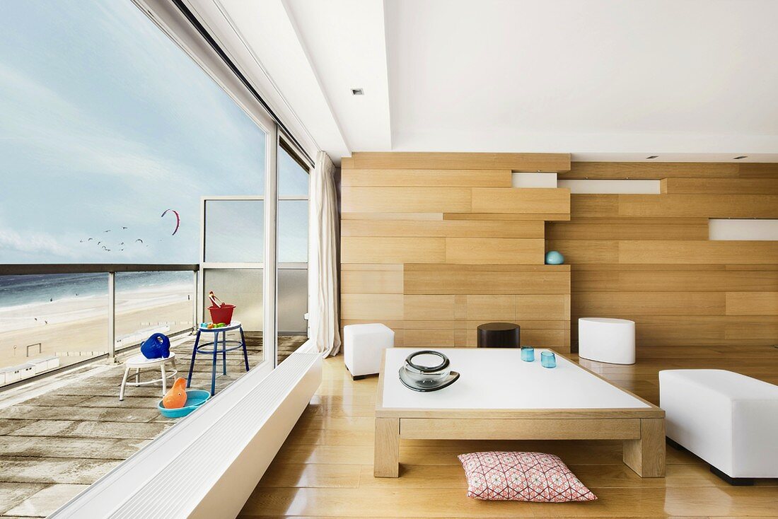 Couchtisch vor Holzpaneelwand im modernen Wohnzimmer mit Panoramablick auf den Strand