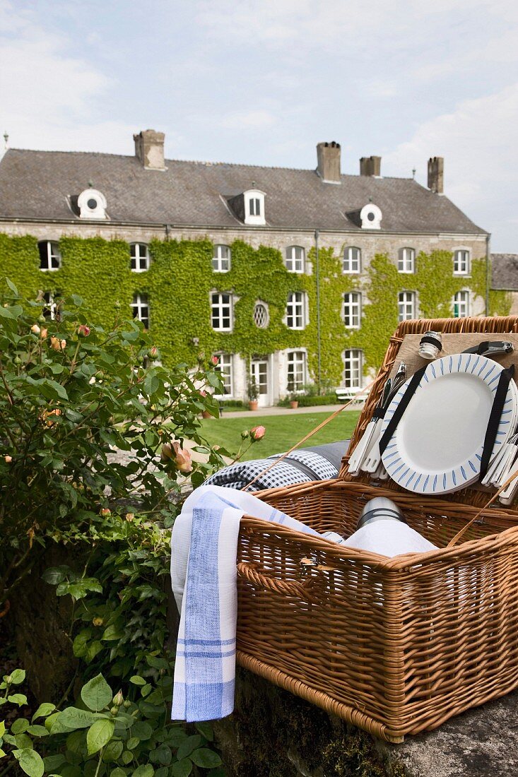 Ein geöffneter Picknickkorb im Vordergrund, dahinter ein altes Herrenhaus im englischen Stil mit efeuberankter Fassade