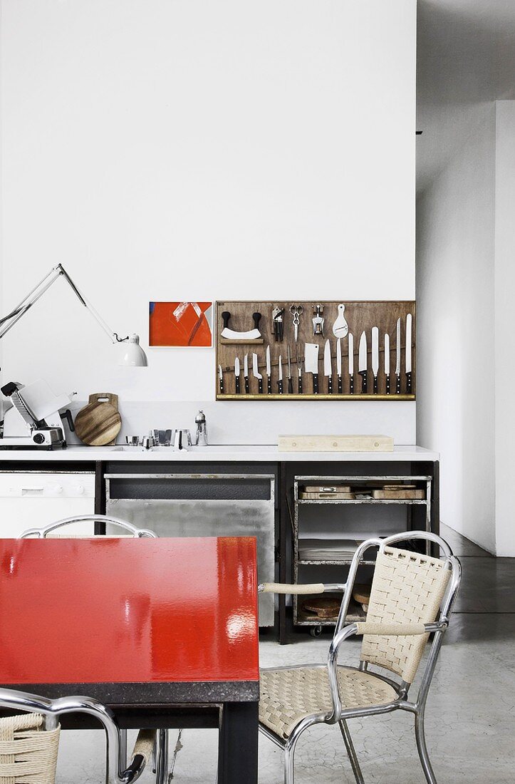 Esstisch mit roter Tischplatte vor einer einfachen Küchenzeile mit Wandhalterung für Küchenmesser