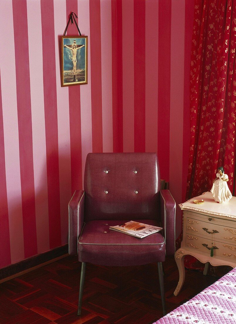 Retrosessel und barockes Nachttischchen vor roter Streifentapete
