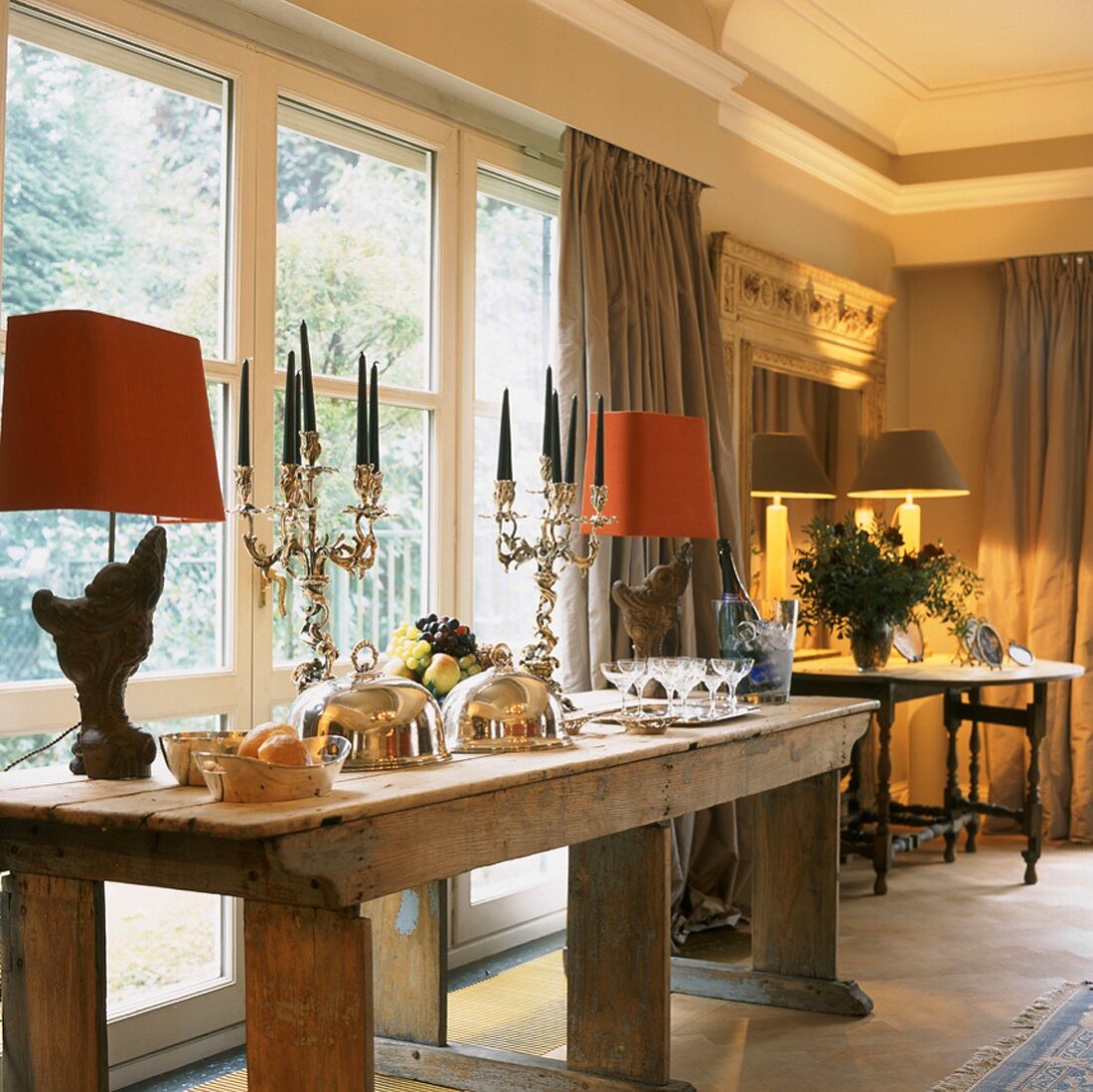 Edles Tafelsilber auf einem rustikalen, antiken Holztisch in einem eleganten Zimmer mit Stuckleiste und Fensterfront
