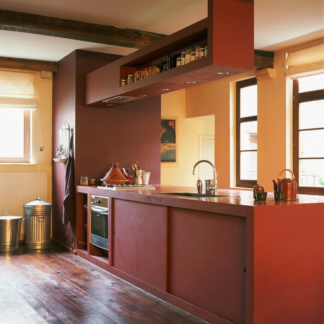 Freistehende, kubische Küchenzeile in Rot in rustikalem Ambiente mit Deckenbalken und Dielenboden