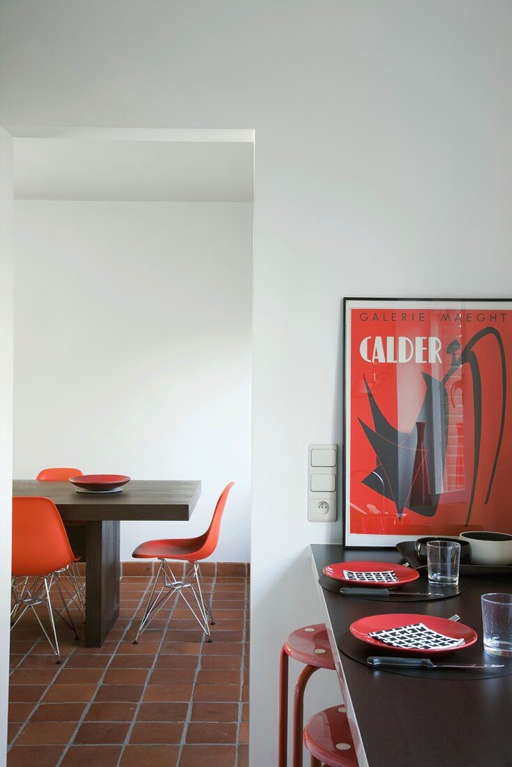 Rote Farbakzente an der gedeckten Küchentheke und dem minimalistischen Esstisch mit Designerstühlen