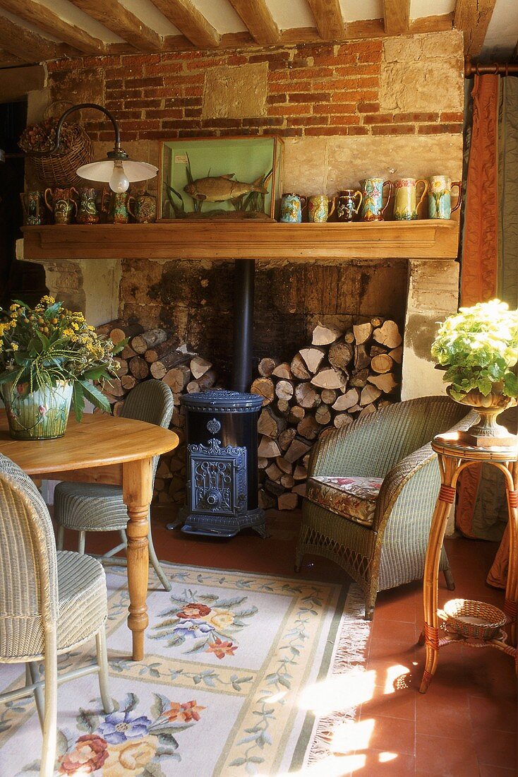 Rattanstühle und Landhaustisch in einem gemütlichen Wohnzimmer mit Kamin, Backsteinwand und Holzbalkendecke