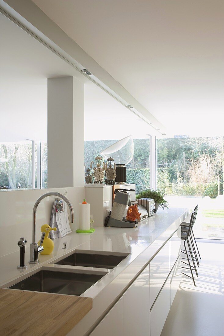 Moderne Küchenzeile mit minimalistischen Hochglanzoberflächen und Blick durch die Fensterfront auf den Garten