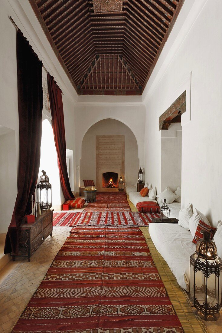 Schlauchförmiger Wohnraum im marokkanischen Stil mit roten Läufern und vielen Sitzgelegenheiten