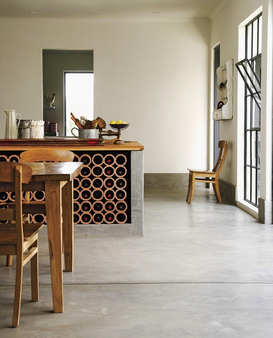 Küchentheke mit Weinregal in einem offenen Wohnraum mit Betonboden und Biedermeierstühlen