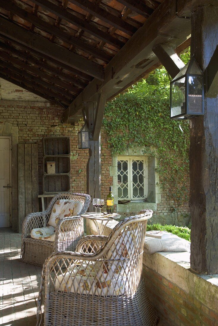 Klassische Korbstühle auf der rustikal überdachten Terrasse eines alten Bauernhauses