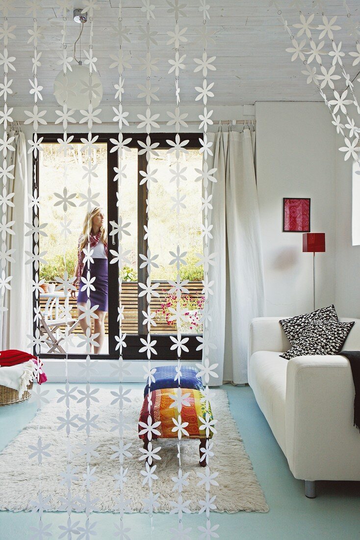 Blick durch floralen Fadenvorhang in modernes Wohnzimmer mit Terrassenzugang und türkisfarbenem Fußboden