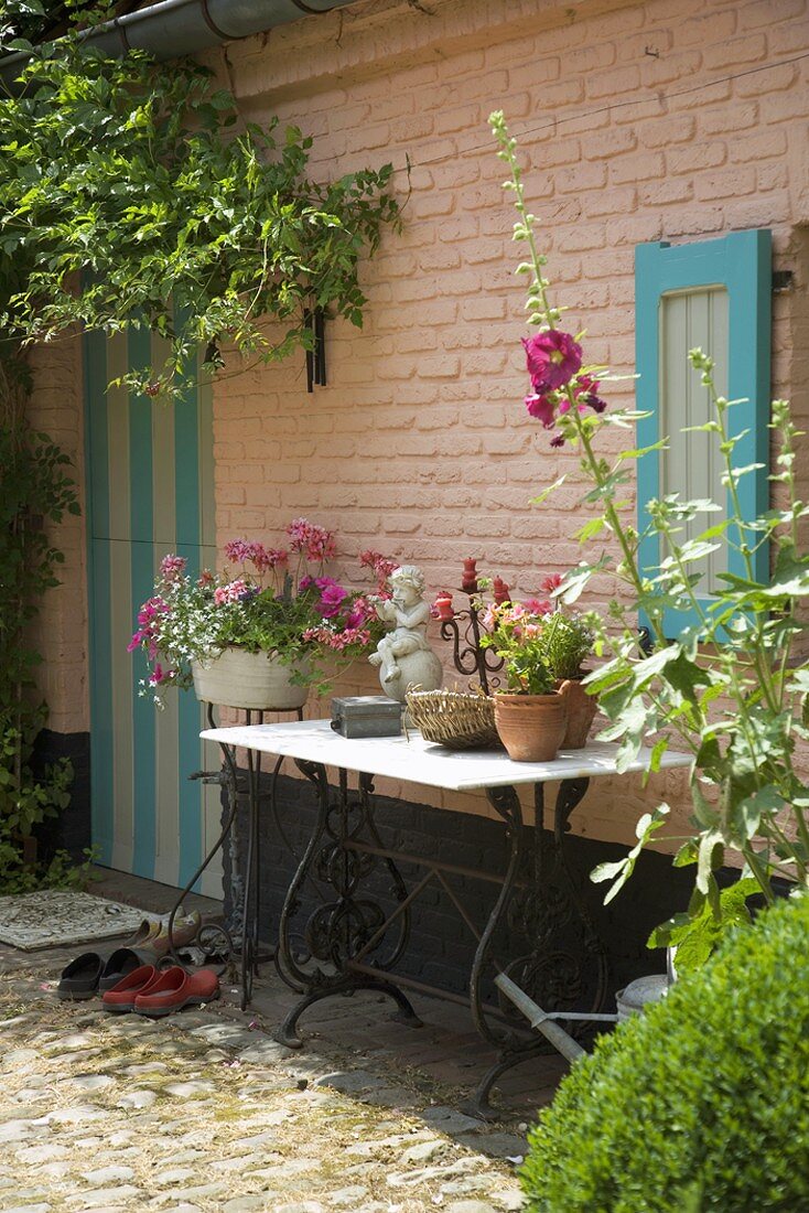 Schöner Vintagegartentisch vor einer bunten Hausfassade aus Backstein in Rosa mit Tür und Fensterladen in Türkis
