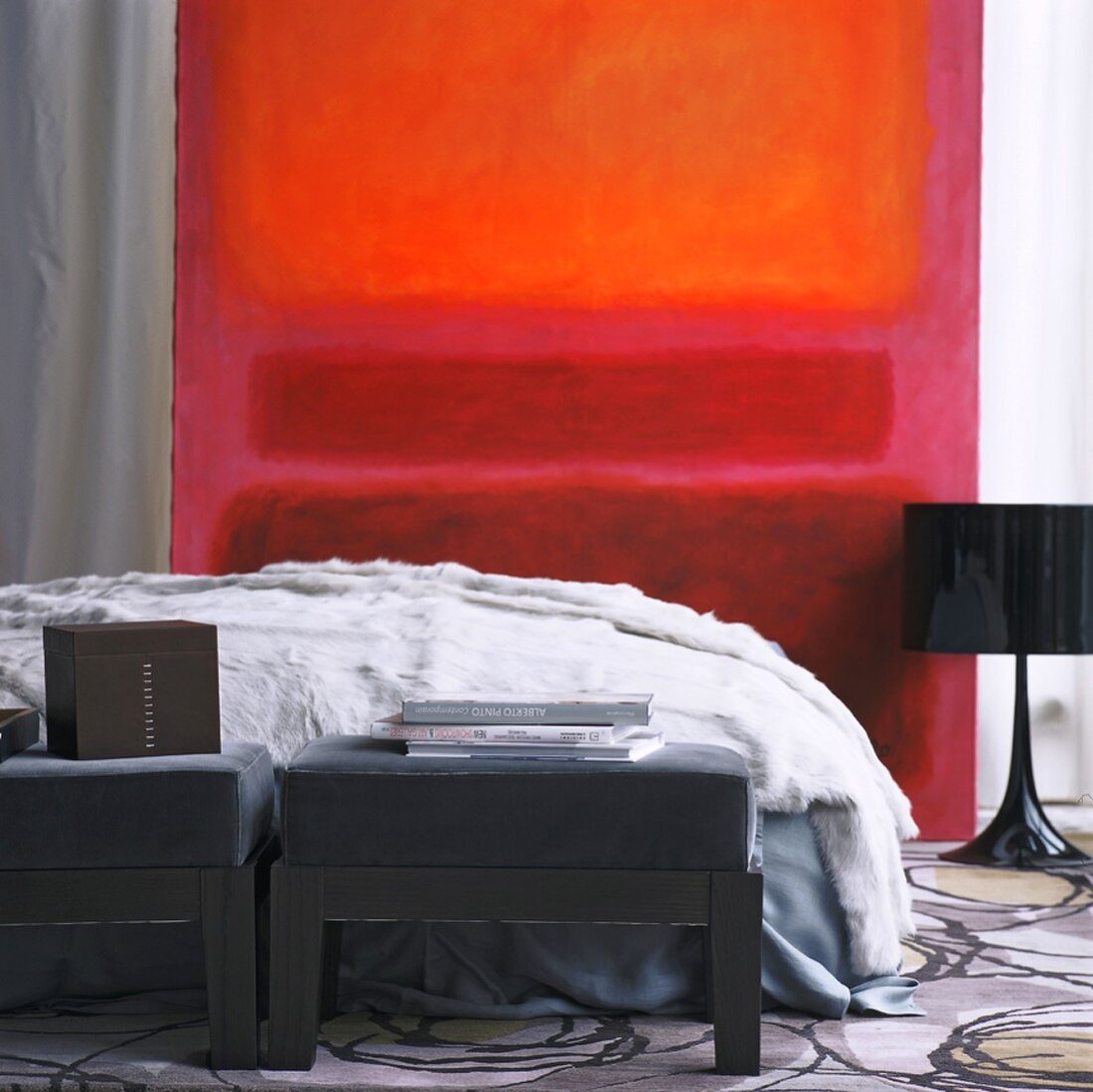 Ausschnitt eines Schlafzimmers mit leuchtendem, rotem Bild und einer schwarzen Retrolampe neben dem Doppelbett mit Felldecke