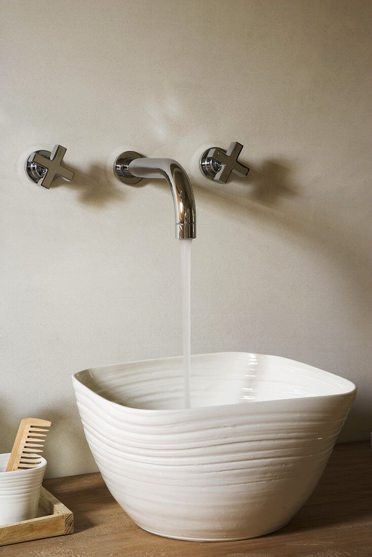 Wasser läuft aus Wandarmatur in Porzellanwaschbecken auf Holzwaschtisch