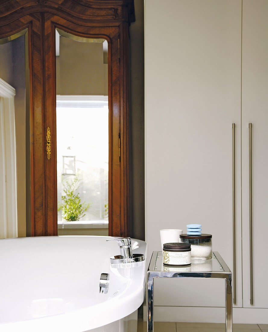 Badewanne mit verchromtem Beistelltisch in modernem Badezimmer; im Hintergrund ein antiker Spiegelschrank