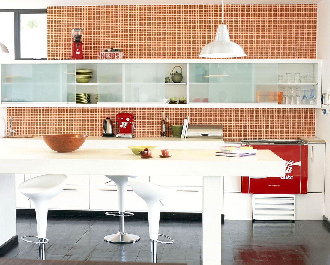 Rot-weiße Küche im Fiftiesstil mit langestreckter Küchenzeile, Hängeschränken, karierter Tapete, Bar & Hockern