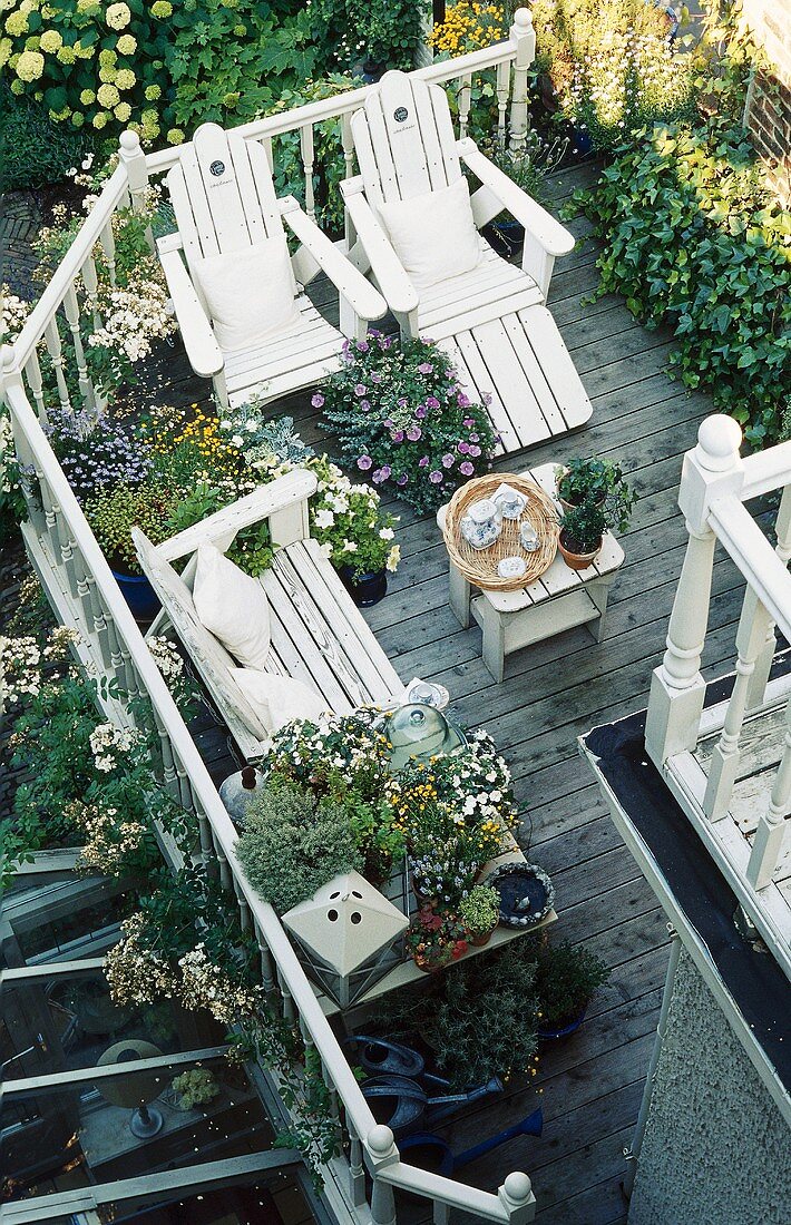 Blick von Oben auf begrünten Holzbalkon mit weißem Holzgeländer & weissen Gartenmöbeln