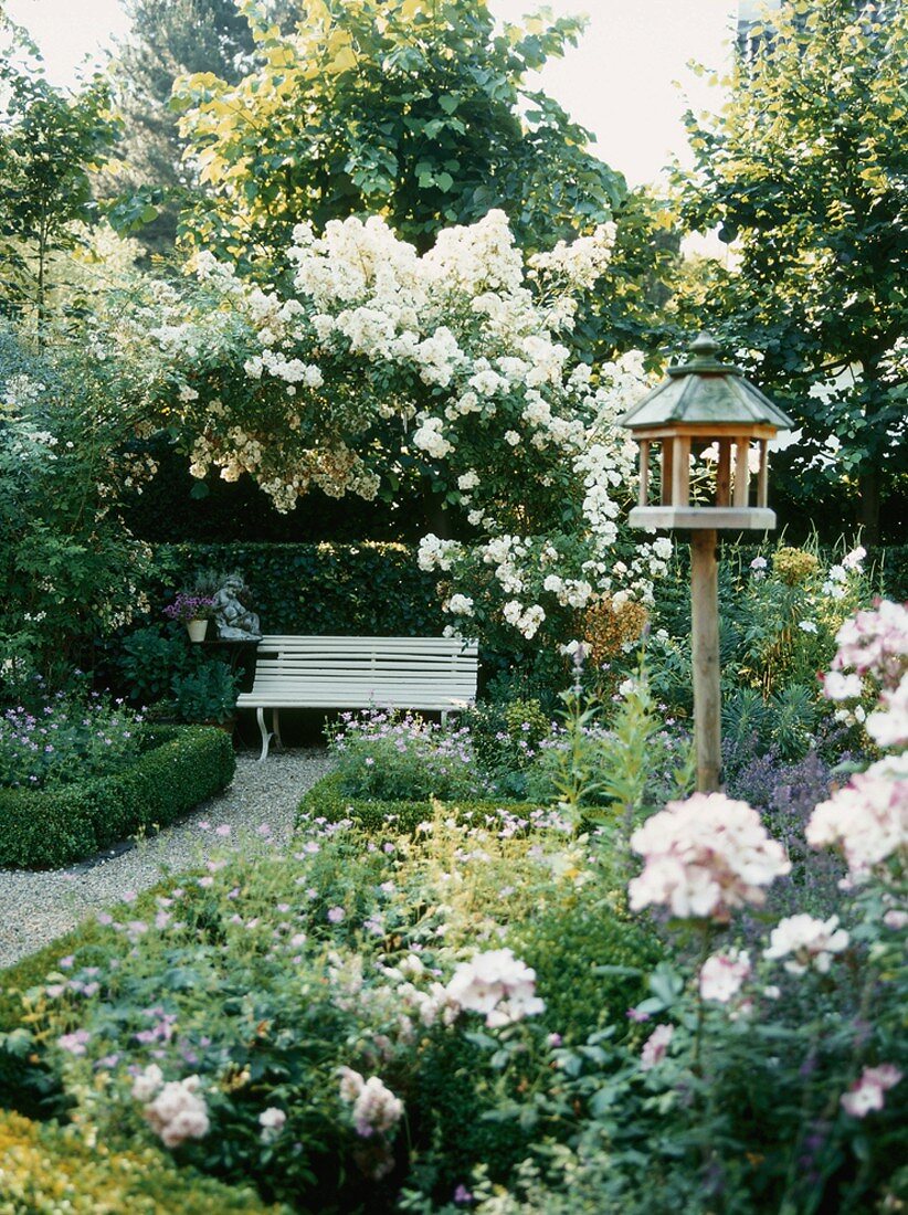 A flowering garden with a bird house and a wooden bench