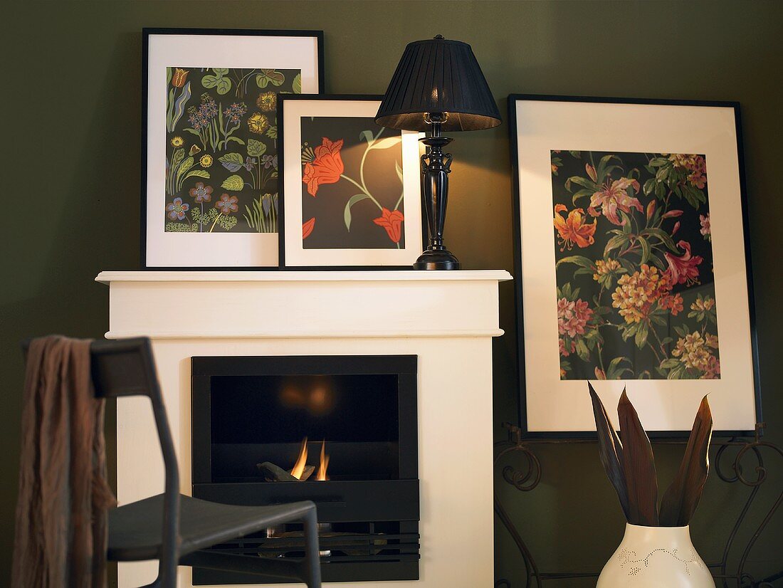 Fireplace with white cornice and table lamps in front of framed pictures of flowers on the wall