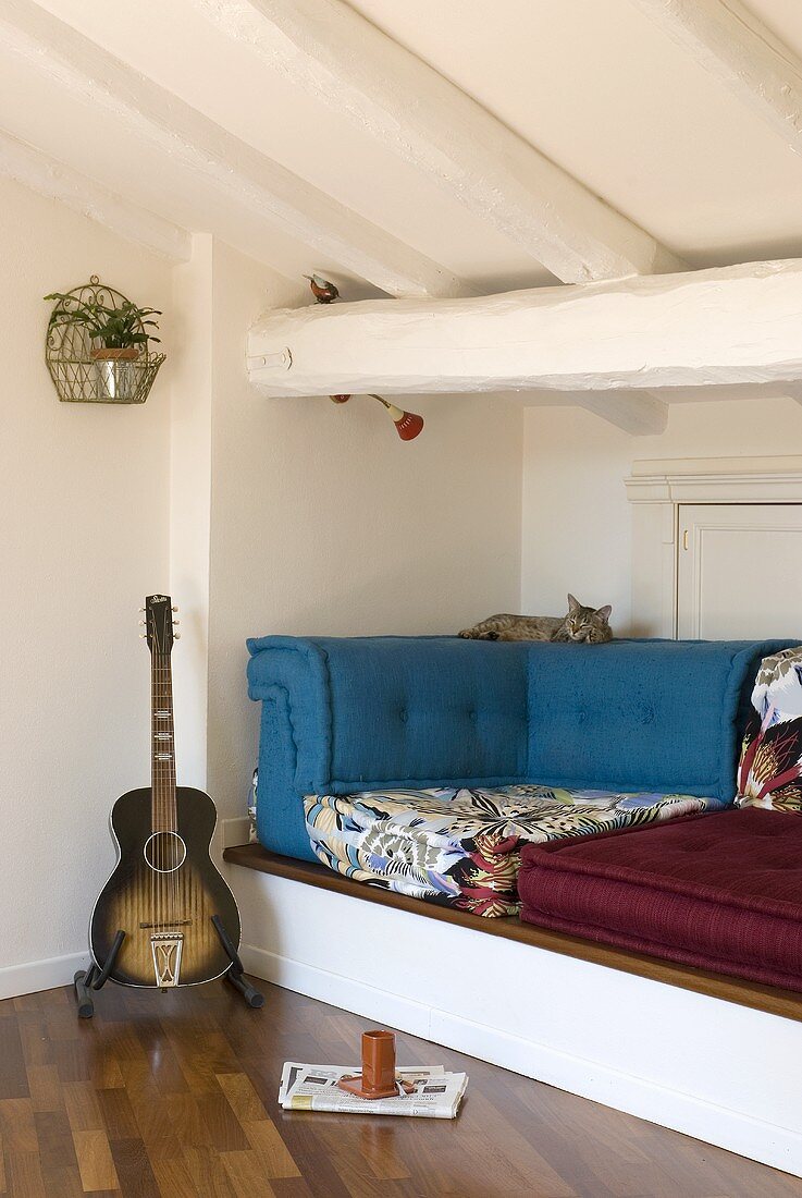 A guitar next to a raised seating corner in an attic room