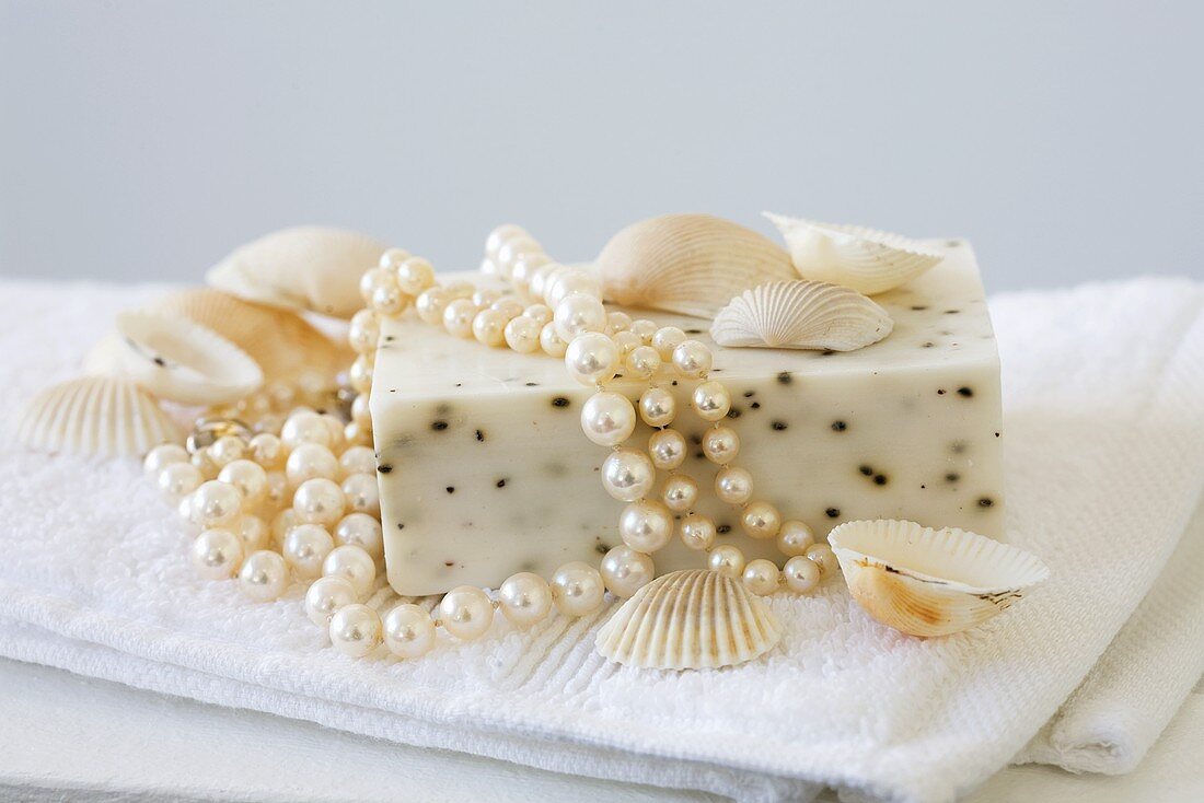 Seife mit Perlen und Muscheln auf weißem Handtuch