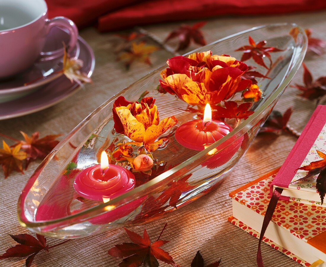 Glasschale mit Blüten von Malerrosen und Schwimmkerzen