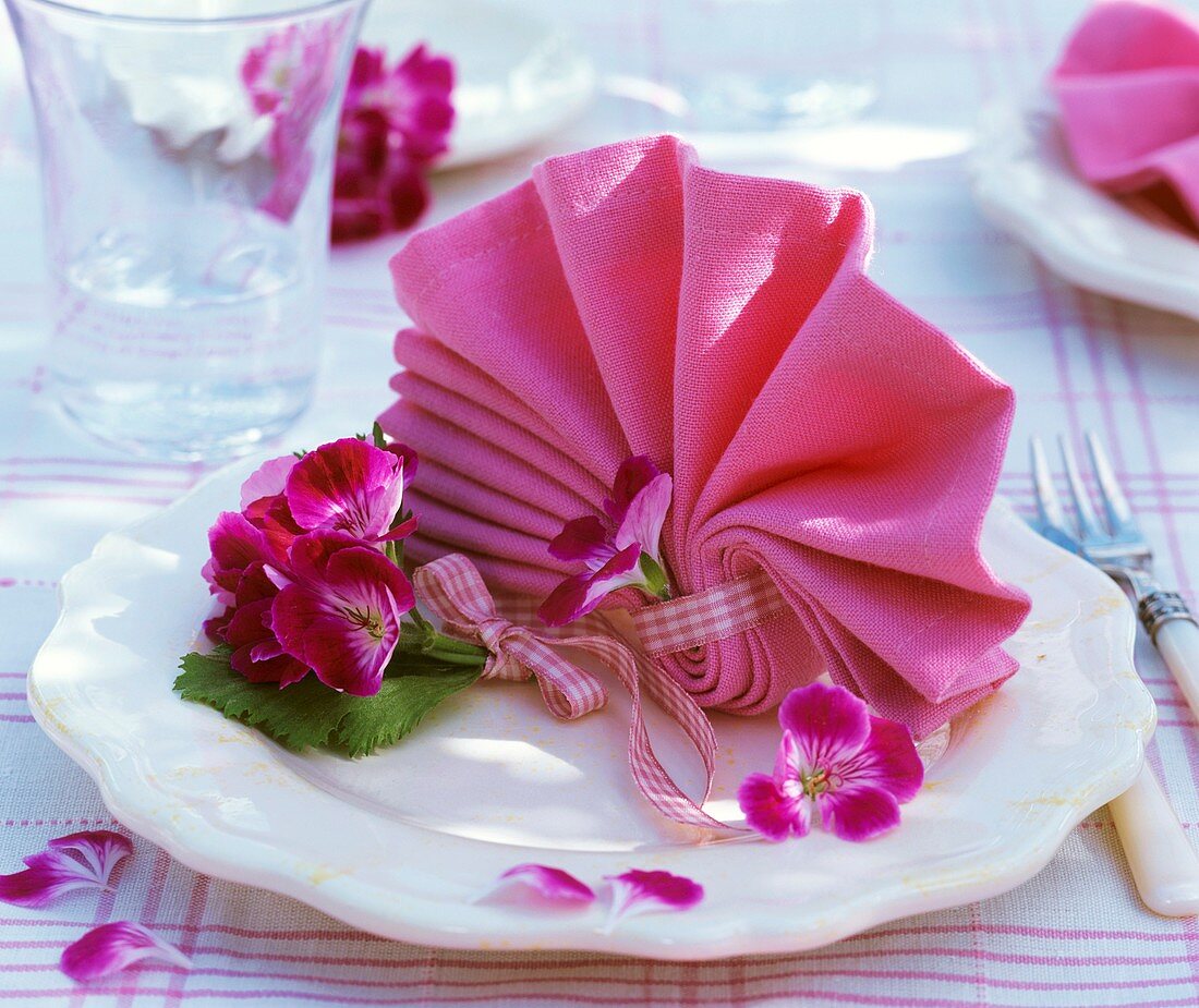 Napkin folded in the shape of a fan with geranium flowers