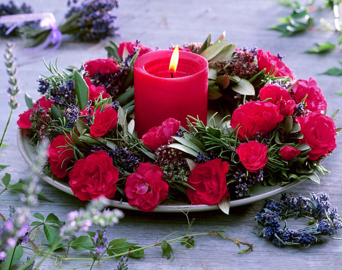 Kranz aus roten Rosen und Kräutern um rote Kerze