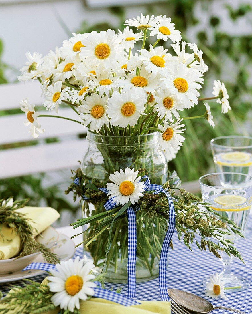 Oxeye daisies in jar with wreath of grasses