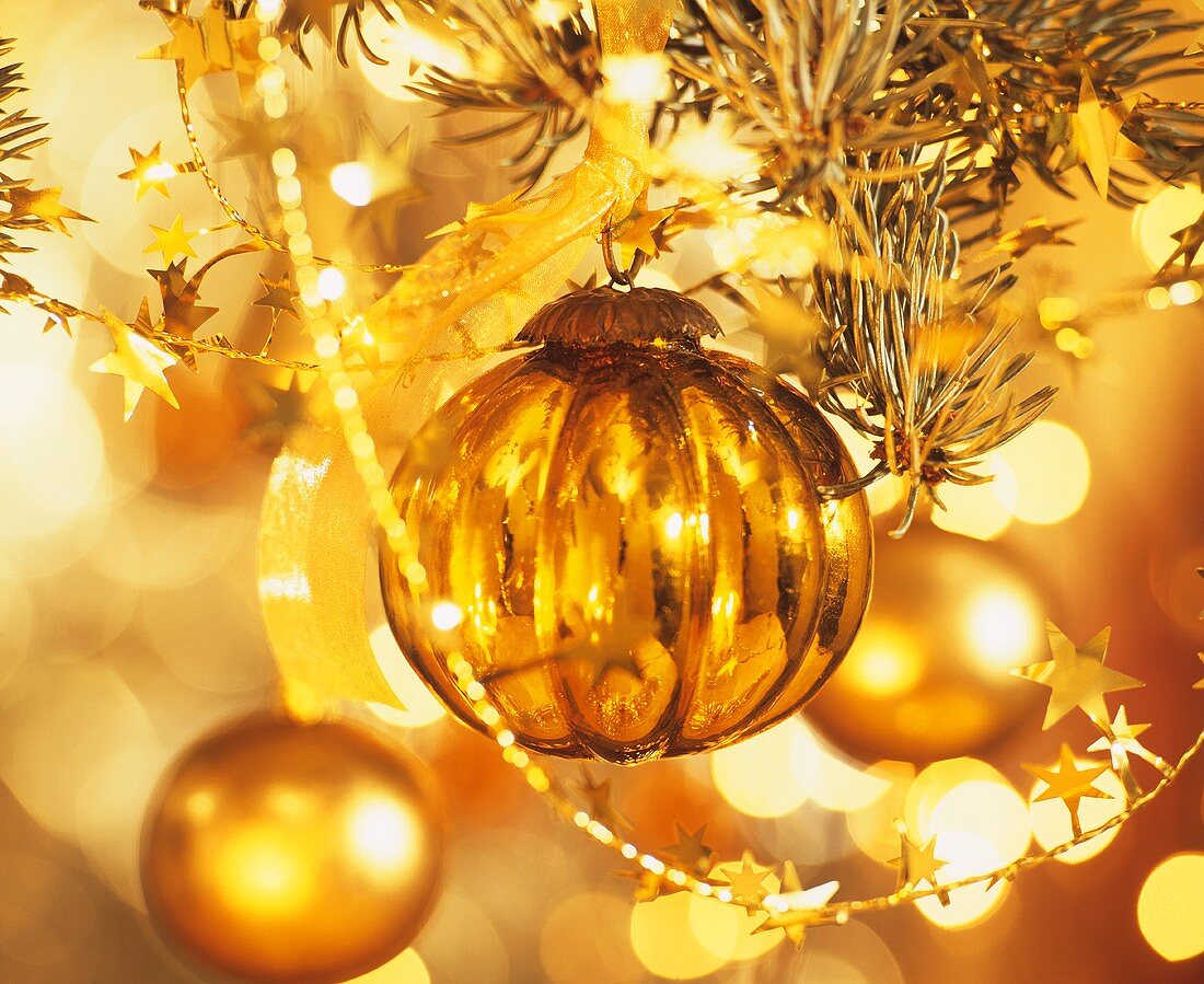 Goldfarbene Weihnachtskugel hängt am Baum