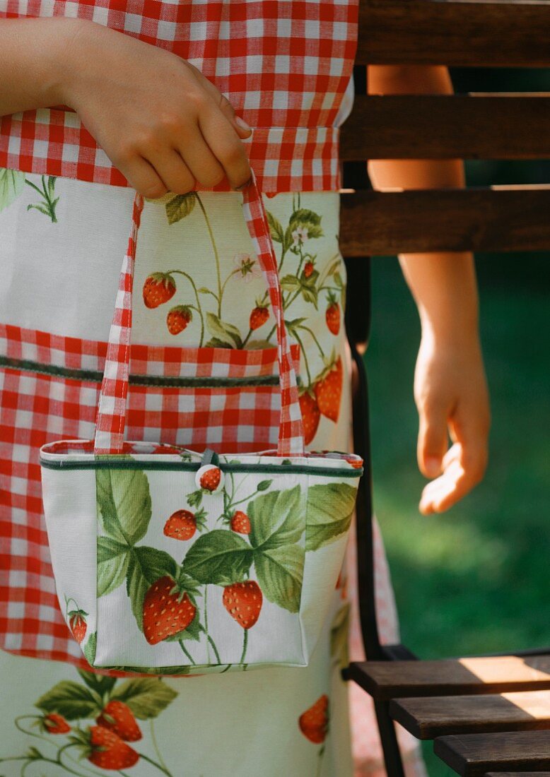 Mädchen trägt Schürze und Tasche mit Erdbeermotiv