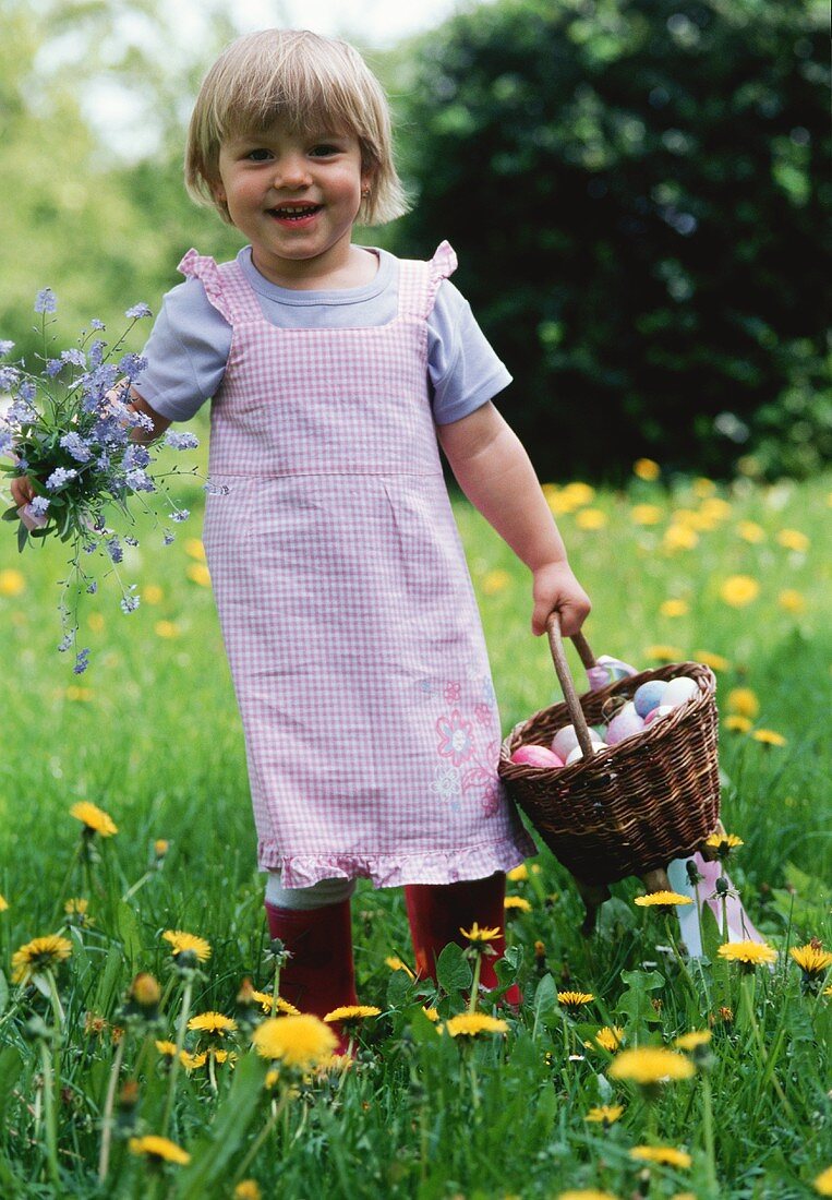 Kleines Mädchen hält Blumen und Korb mit Ostereiern