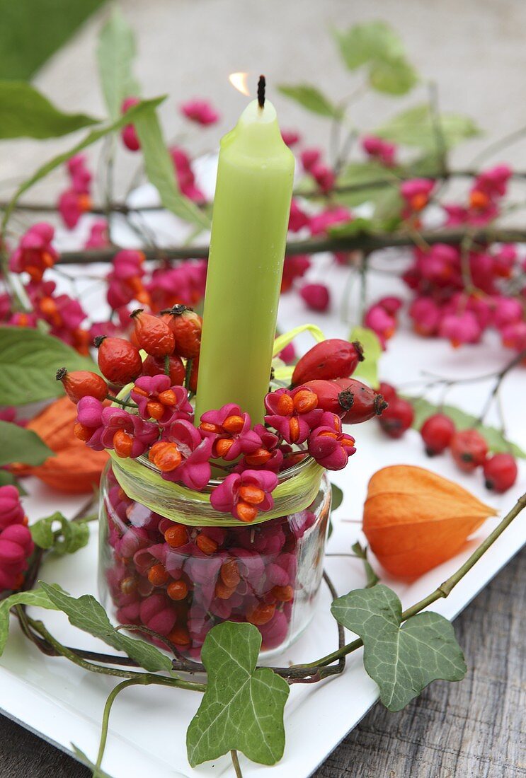 A candle in a glass with spindle and rosehips decorating the table