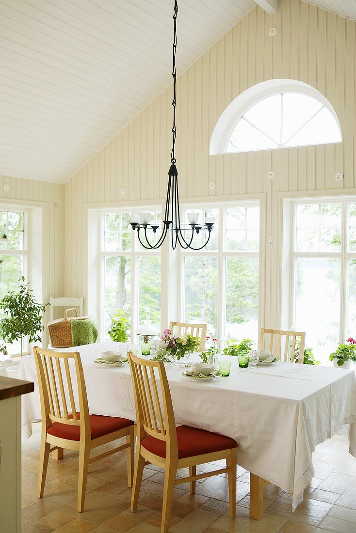 Gedeckter Esstisch in Wohnraum mit Holzvertäfelung, breiter Fensterfront & Rundbogenfenster