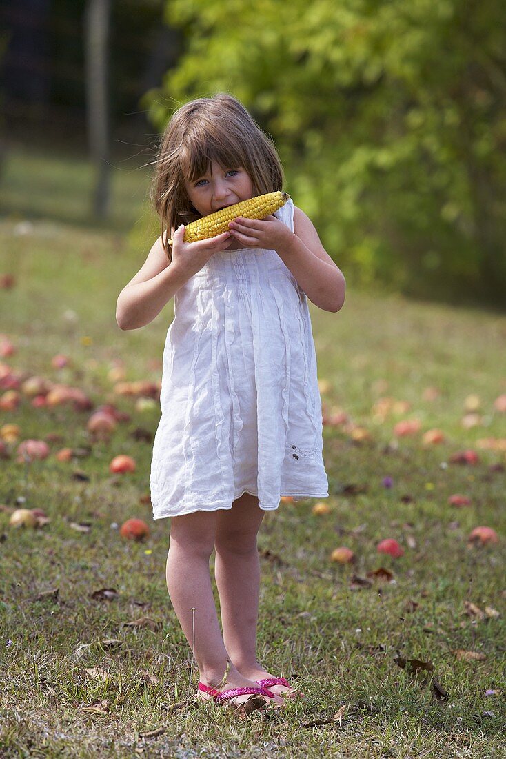 Mädchen isst Maiskolben im Garten