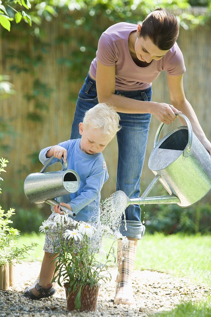 A mother and son watering the flowers in a garden