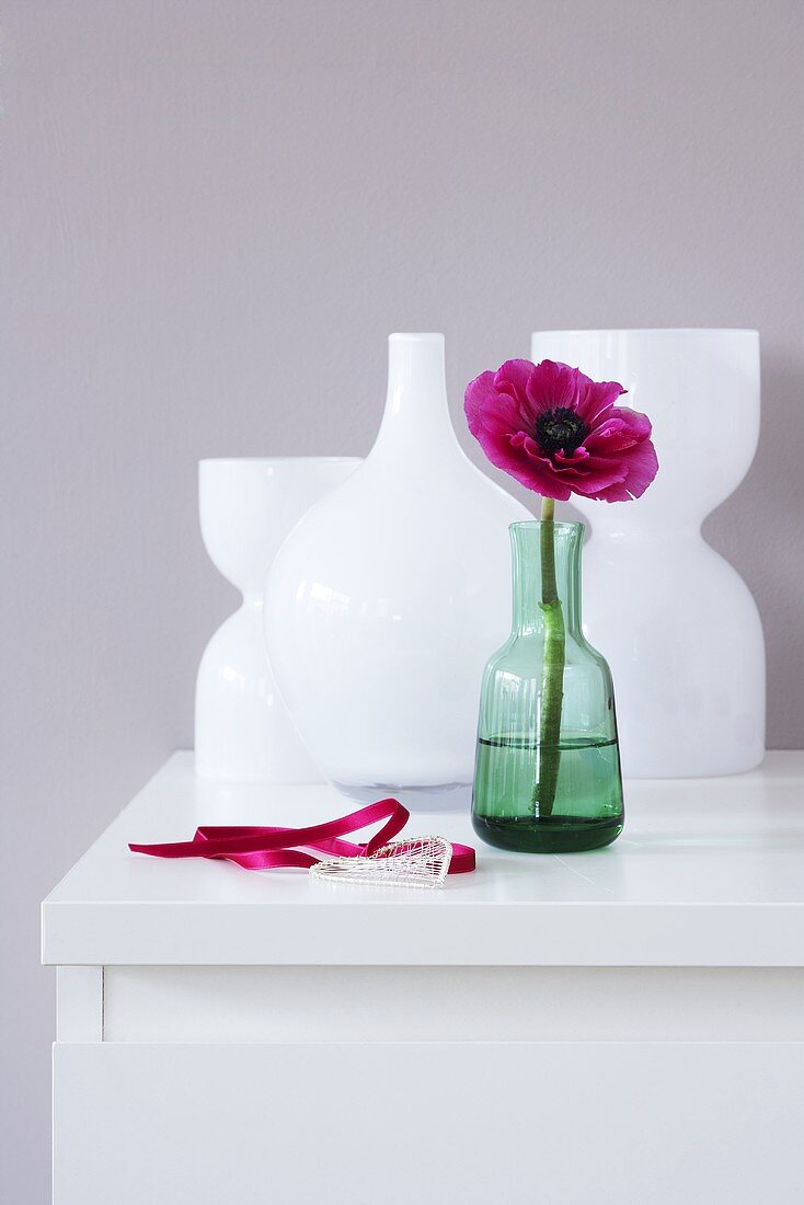 White vases and a green vase with a flower in it